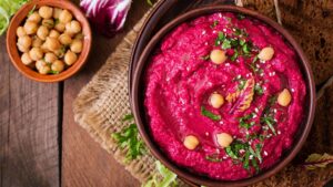 A beetroot and chickpea puree dish topped with herbs and seeds in a brown dish and a side dish of more chickpeas on the rustic wooden table