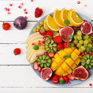 A plate of fresh fruits cut ready to eat including mango strawberries orange figs grapes kiwi fruit pear mint leaves